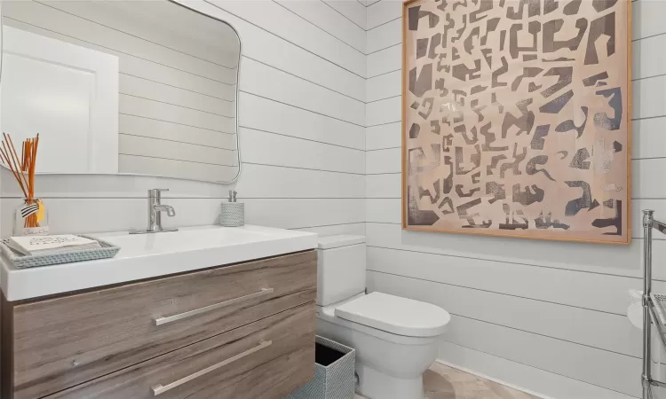 Bathroom with toilet, wooden walls, and vanity