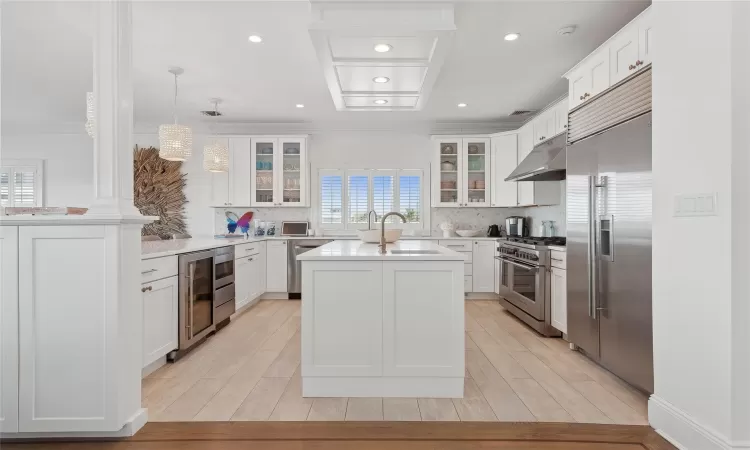 Kitchen featuring sink, white cabinets, built in appliances, and pendant lighting