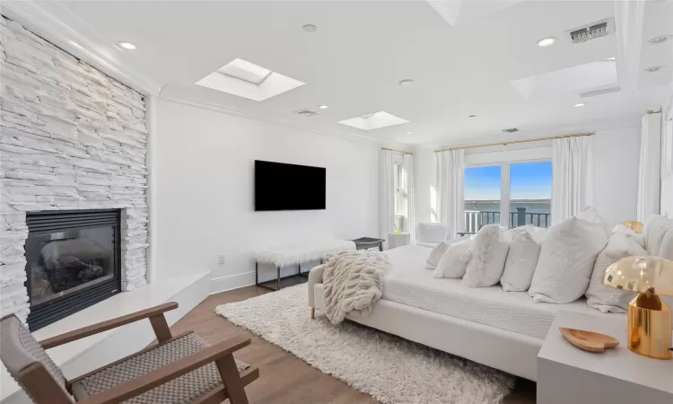 Bedroom with a fireplace, a skylight, hardwood / wood-style floors, and crown molding