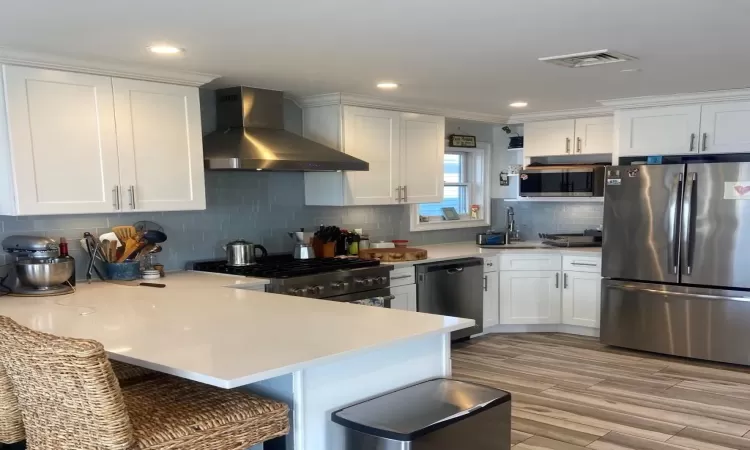 Kitchen with wall chimney range hood, white cabinetry, and stainless steel appliances