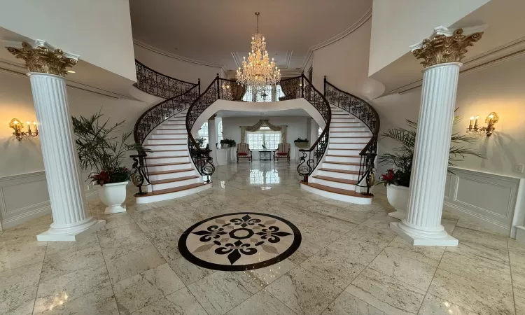 Entrance foyer featuring a high ceiling, a notable chandelier, decorative columns, and ornamental molding