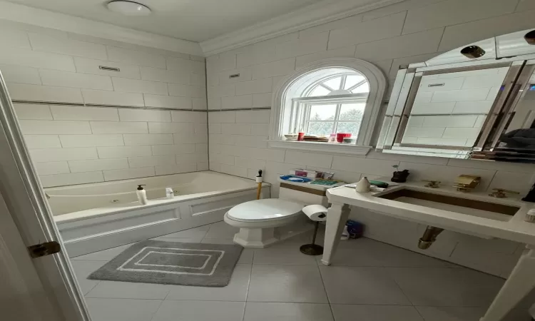 Bathroom featuring crown molding, tile patterned floors, washtub / shower combination, toilet, and tile walls