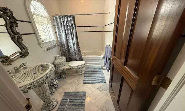 Bathroom featuring toilet, shower / bathtub combination with curtain, and tile walls