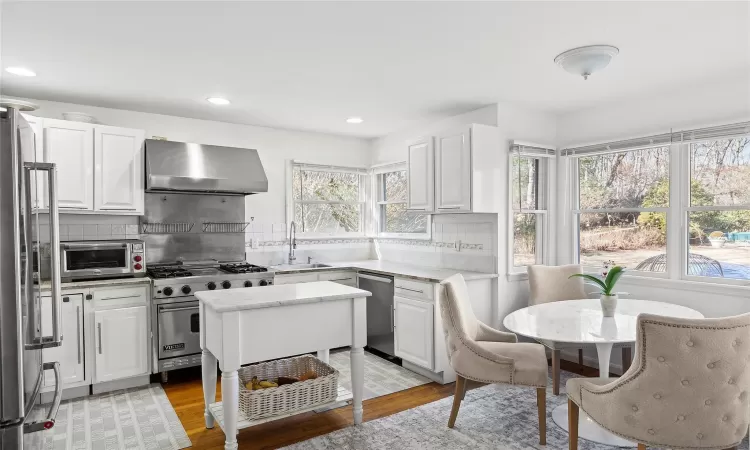 Kitchen with premium appliances, a sink, wall chimney exhaust hood, light countertops, and white cabinets