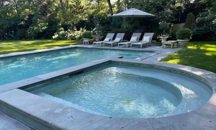 View of pool featuring a lawn and a pool with connected hot tub