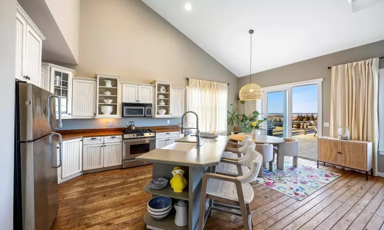 Kitchen featuring stainless steel appliances, glass insert cabinets, hanging light fixtures, and open shelves