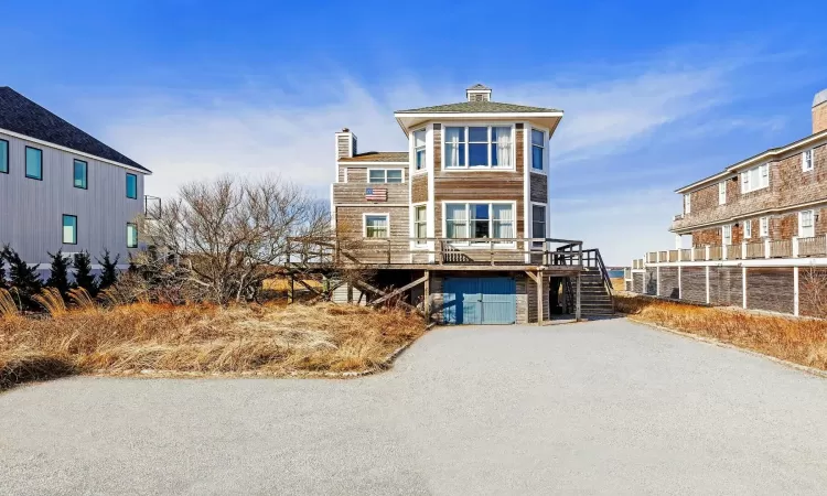 View of front facade featuring driveway, stairs, a chimney, and a deck