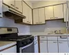 Kitchen featuring white cabinets, gas range, light countertops, under cabinet range hood, and a sink