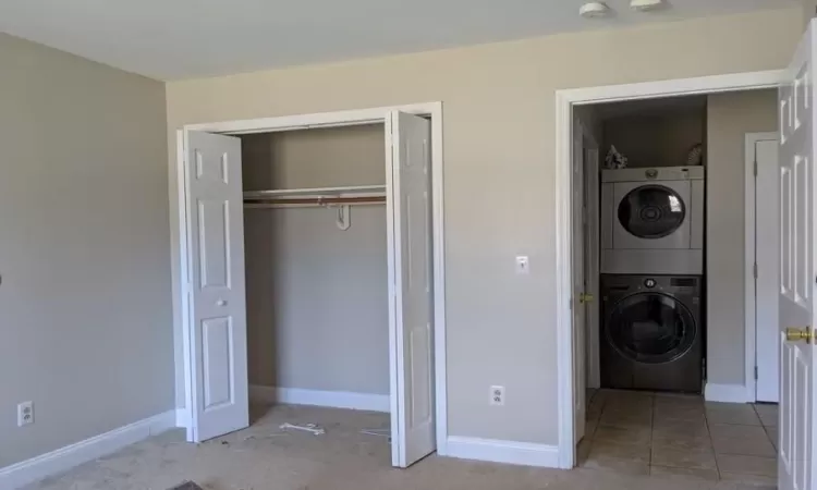 Unfurnished bedroom featuring stacked washer / drying machine, a closet, light tile patterned flooring, and baseboards