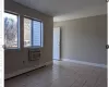 Empty room with light tile patterned floors, baseboards, baseboard heating, and an AC wall unit