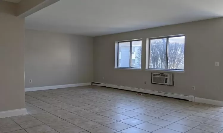 Empty room featuring a baseboard heating unit, light tile patterned floors, a wall unit AC, and baseboards