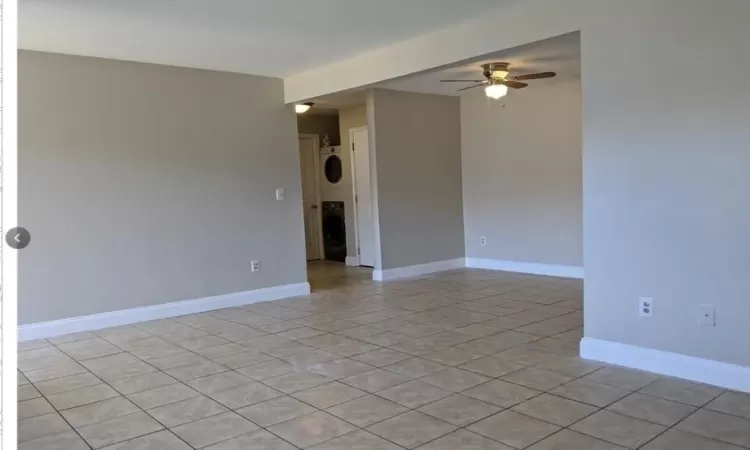 Unfurnished room featuring stacked washer and dryer, light tile patterned floors, baseboards, and a ceiling fan