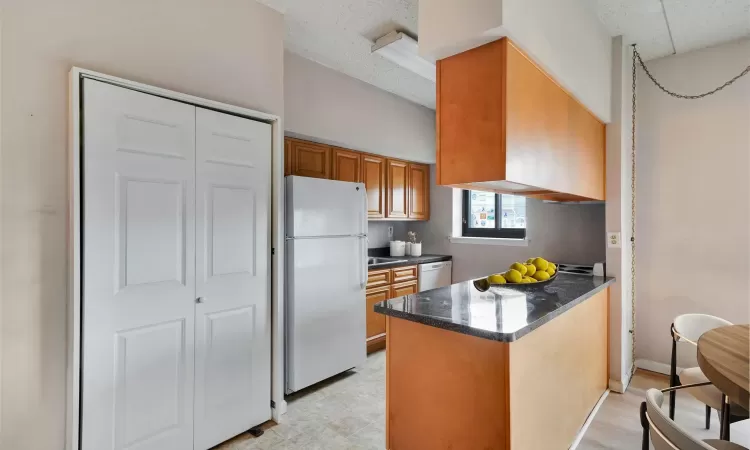 Kitchen featuring dark stone counters, a peninsula, white appliances, and brown cabinets