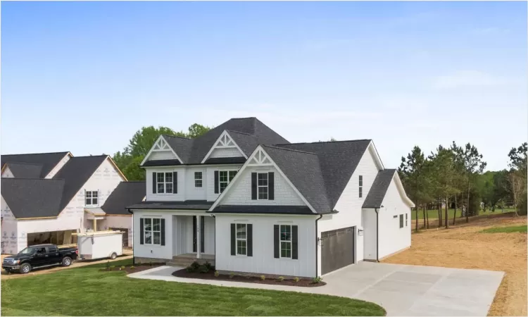 View of front of property featuring board and batten siding, a garage, a front lawn, and concrete driveway