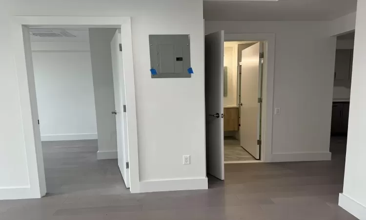 Hallway with light wood finished floors, baseboards, electric panel, and visible vents