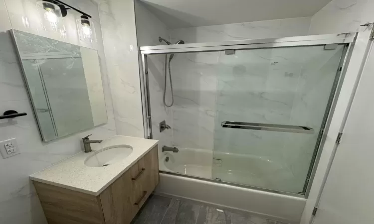 Full bathroom with bath / shower combo with glass door, tile walls, and vanity