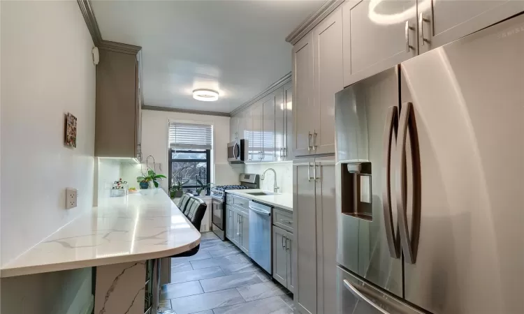 Kitchen with stainless steel appliances, gray cabinets, and light stone countertops