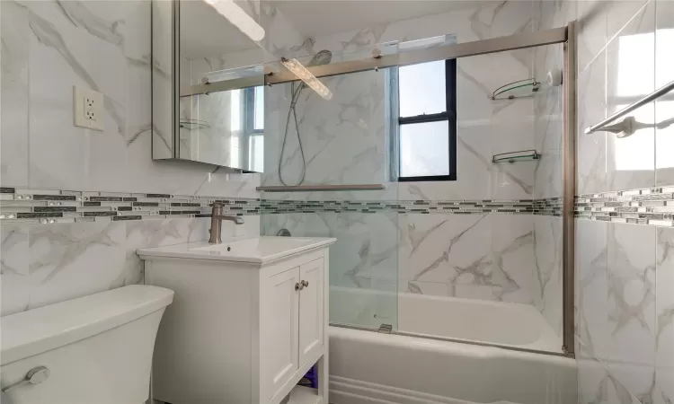 Full bathroom with toilet, bath / shower combo with glass door, vanity, and a wealth of natural light