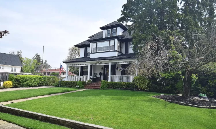 View of front of house with covered porch, a front lawn, and roof with shingles