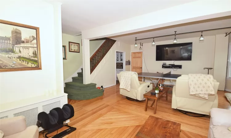 Living area featuring baseboards, radiator heating unit, parquet floors, rail lighting, and stairs