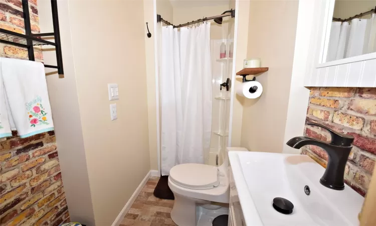 Bathroom with curtained shower, toilet, brick wall, a sink, and baseboards