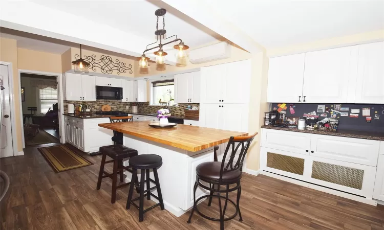 Kitchen featuring butcher block counters, white cabinetry, black microwave, and decorative light fixtures