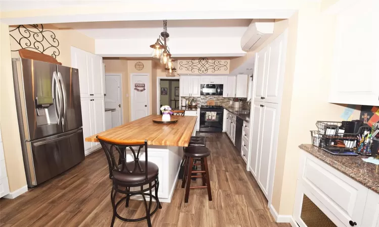 Kitchen with a kitchen breakfast bar, black appliances, decorative light fixtures, and white cabinets