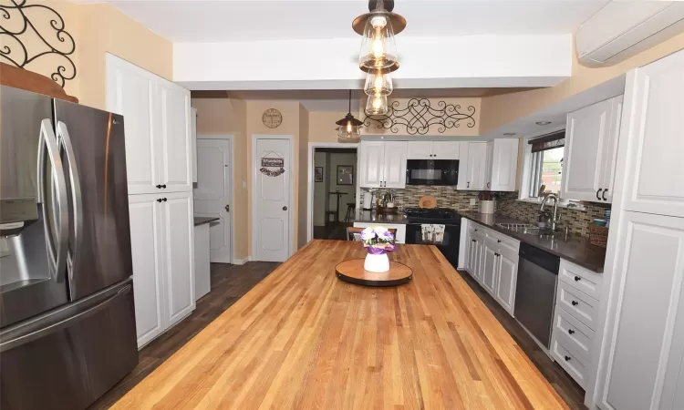 Kitchen with a wall unit AC, decorative light fixtures, white cabinets, a sink, and black appliances