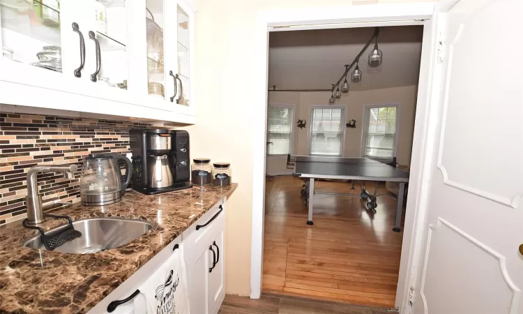 Kitchen featuring dark wood-style floors, a sink, white cabinets, dark stone counters, and tasteful backsplash