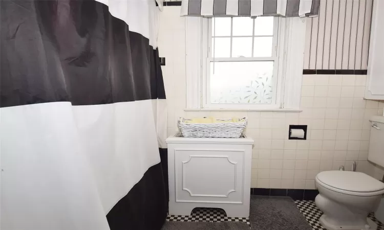 Bathroom with toilet, tile patterned flooring, and tile walls