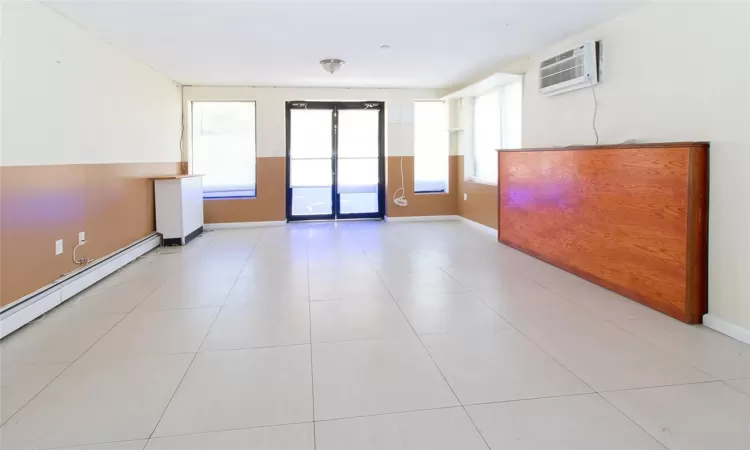 Spare room featuring light tile patterned floors, a wall mounted air conditioner, a baseboard radiator, and baseboards