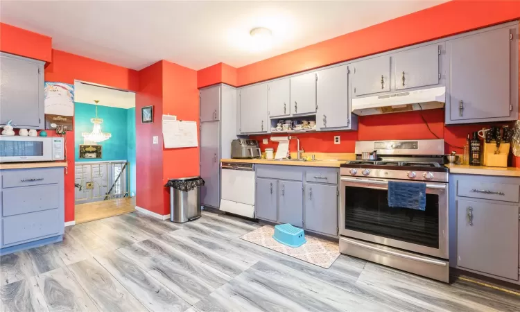 Kitchen featuring light countertops, hanging light fixtures, a sink, white appliances, and under cabinet range hood