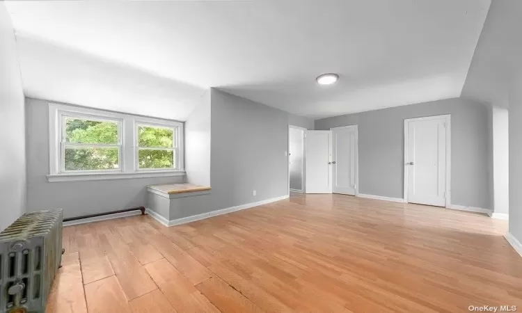 Additional living space with vaulted ceiling, light wood finished floors, radiator heating unit, and baseboards