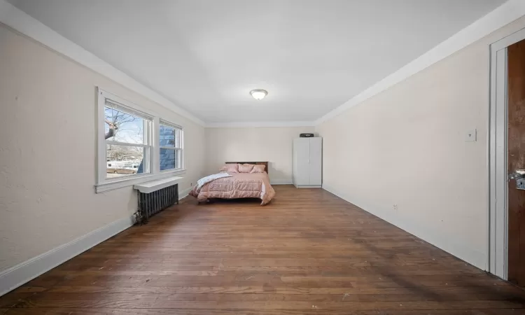 Bedroom with dark hardwood / wood-style flooring, crown molding, and radiator heating unit