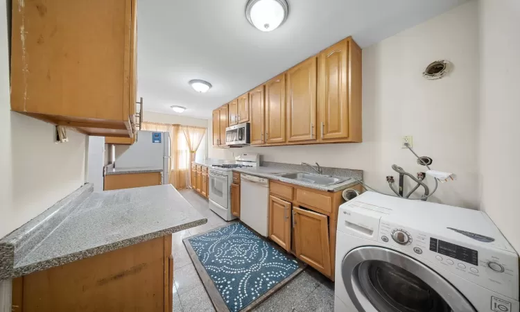 Kitchen with white appliances, sink, washer / clothes dryer, and light stone countertops