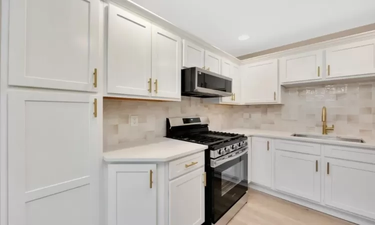 Kitchen featuring white cabinets, sink, light hardwood / wood-style flooring, appliances with stainless steel finishes, and tasteful backsplash