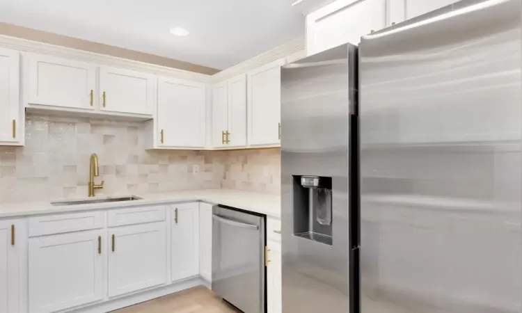 Kitchen featuring backsplash, sink, light hardwood / wood-style flooring, white cabinetry, and stainless steel appliances