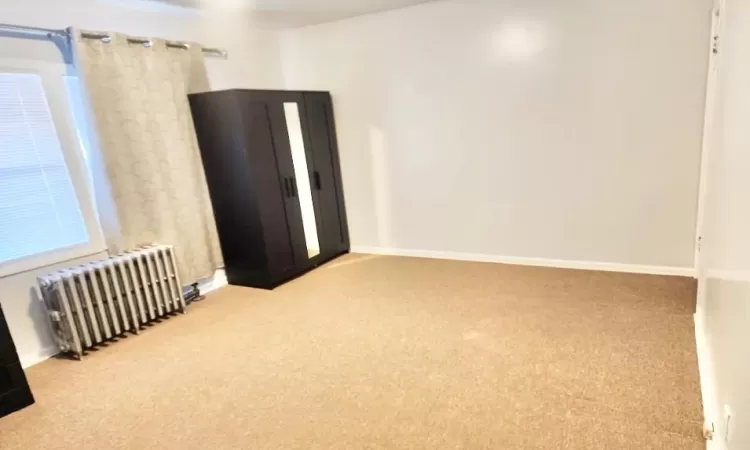 Carpeted empty room with radiator heating unit and baseboards