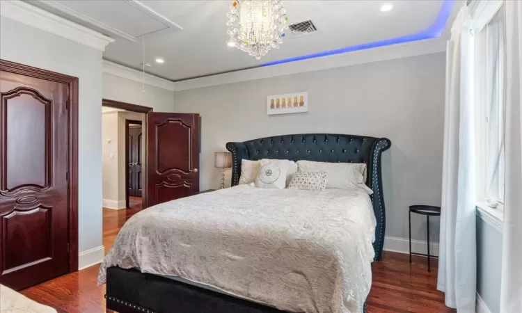 Bedroom featuring attic access, visible vents, wood finished floors, and ornamental molding