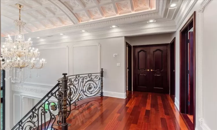 Hallway featuring dark wood-style floors, crown molding, an upstairs landing, a chandelier, and recessed lighting