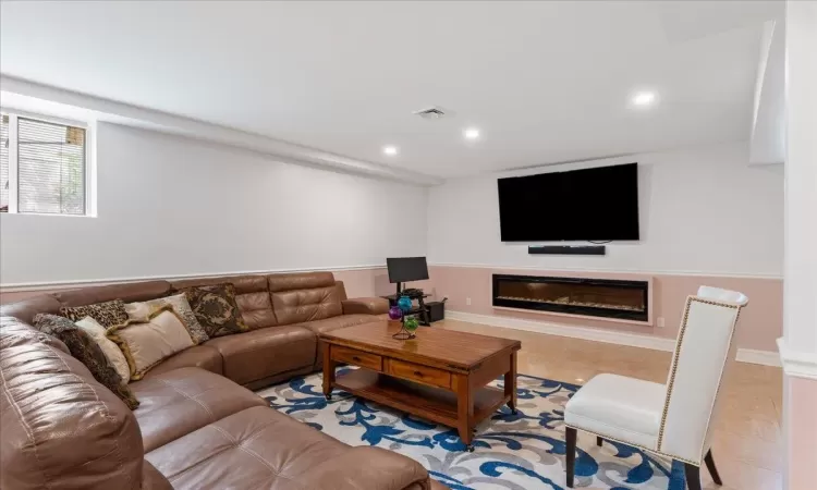 Living area with light tile patterned floors, recessed lighting, visible vents, and a glass covered fireplace