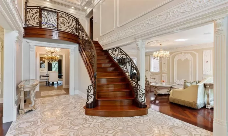 Staircase with baseboards, a towering ceiling, ornamental molding, ornate columns, and a notable chandelier