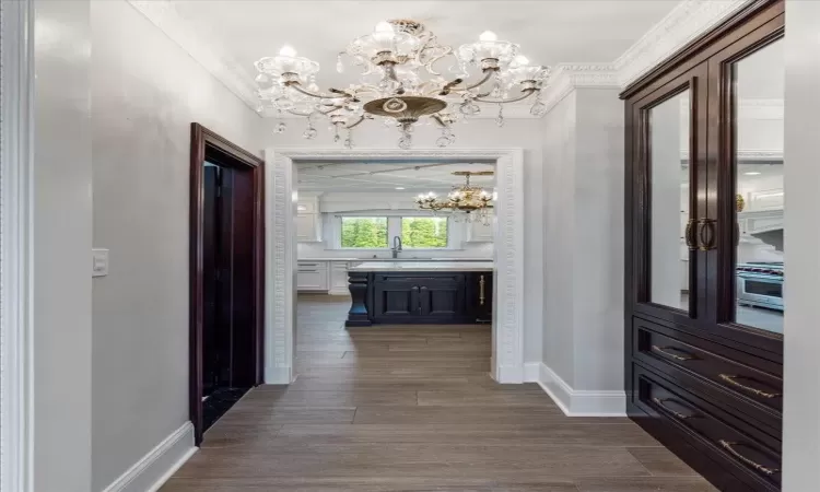 Hall with ornamental molding, dark wood-style flooring, a notable chandelier, and baseboards