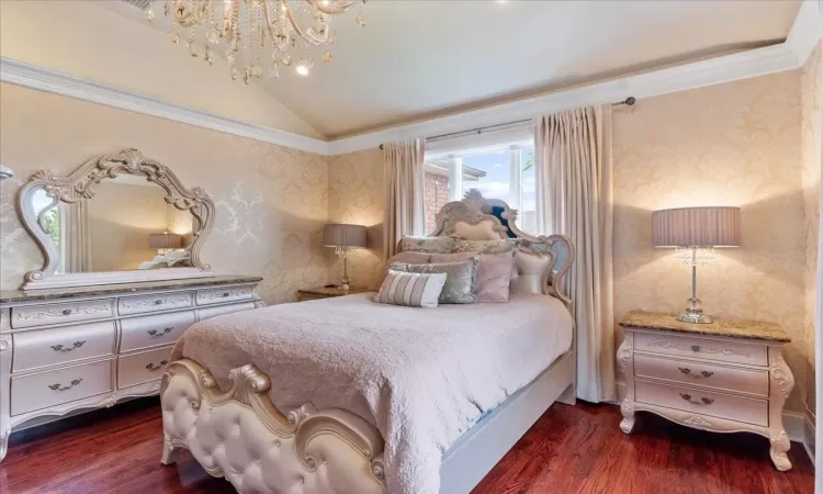 Bedroom featuring vaulted ceiling, dark wood-type flooring, a notable chandelier, and wallpapered walls