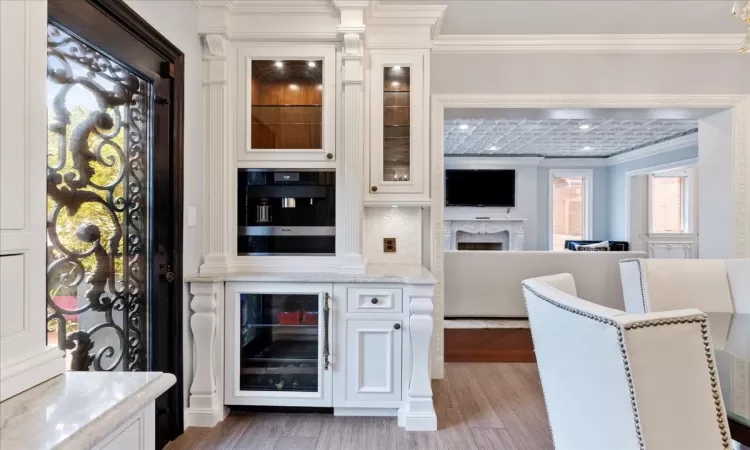 Bar with wall oven, light wood finished floors, tasteful backsplash, wine cooler, and ornamental molding