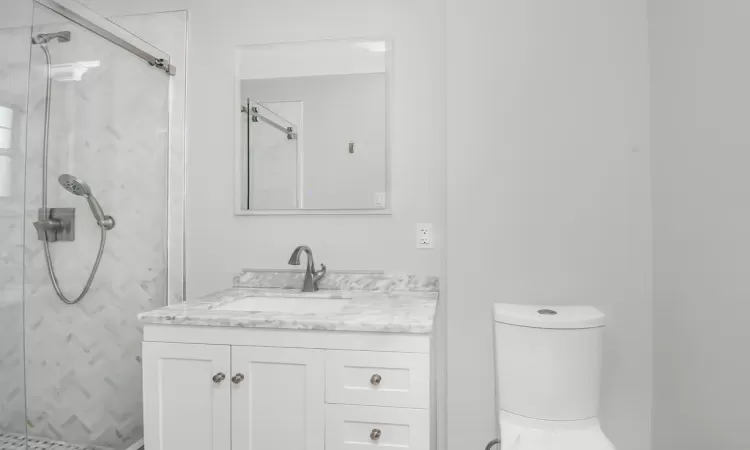 Bathroom with toilet, vanity, and a marble finish shower