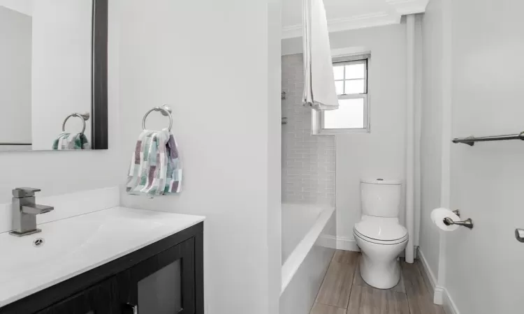 Bathroom featuring wood finish floors, shower / bathtub combination, toilet, vanity, and baseboards