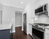 Kitchen with dark wood-style flooring, white cabinetry, appliances with stainless steel finishes, decorative backsplash, and crown molding