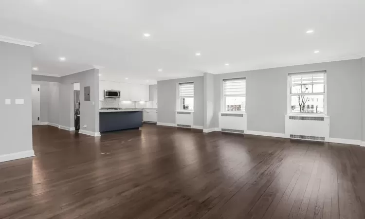 Unfurnished living room featuring dark wood-type flooring, radiator, and crown molding