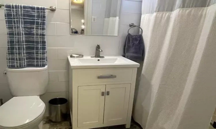 Bathroom featuring toilet, tile walls, and vanity